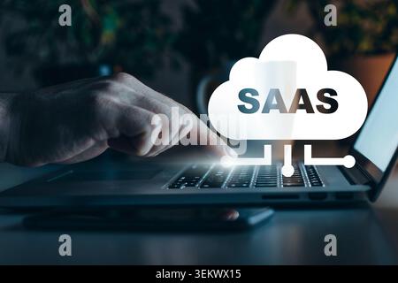 Hand pointing at a laptop keyboard with Saas concept on the screen in a dark room Stock Photo