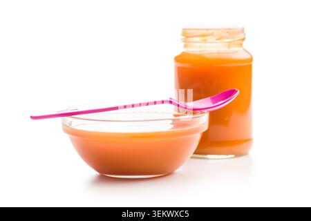 Creamy orange baby food puree presented in a glass jar and bowl with a pink spoon on a white background, evoking homemade feeding, infant nutrition, w Stock Photo