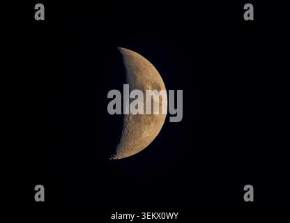 Moon displaying its first quarter phase in a dark night sky, revealing details of its craters and lunar surface against cosmic blackness Stock Photo