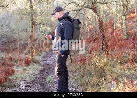 Man with backpack checking his smartphone for directions on a hiking trail Stock Photo
