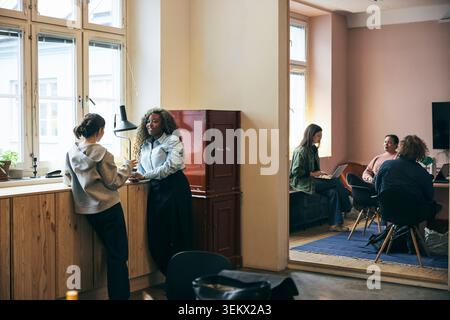 Female business professionals talking with each other while standing near window table in tech office Stock Photo