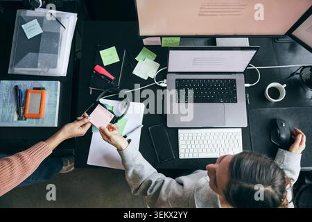 Directly above view of female entrepreneur passing adhesive note to colleague while sitting at desk in office Stock Photo