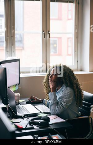 Concentrated female business professional analyzing data preview on dual monitor in startup office Stock Photo