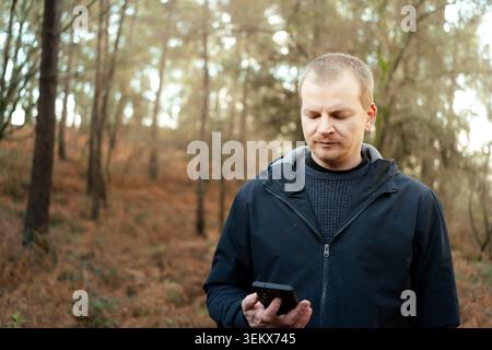 Man holding mobile phone while standing outdoors in the woods Stock Photo