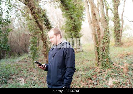 Man holding a mobile phone while standing among trees and green vegetation Stock Photo