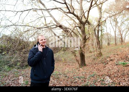 Man smiling, having a conversation on his mobile device in a natural outdoor environment Stock Photo