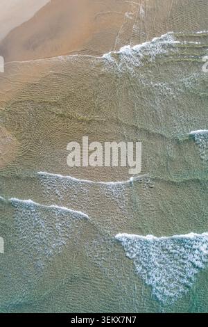Peaceful drone shot of shallow sea water moving slowly over the golden sand on a sunny day Stock Photo