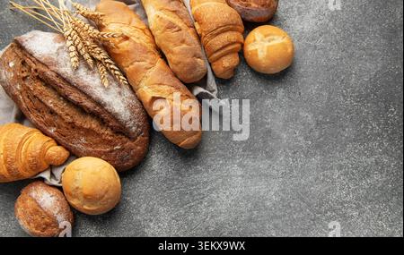 Assortment of fresh baked bread, baguettes, buns, and croissants on a gray backdrop Stock Photo