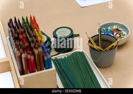 Supplies for arts and crafts, including coloured pencils, floral tape, wire stems and push pins, are organised on the table. Stock Photo