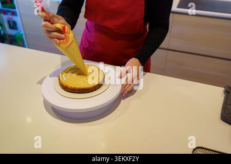 Baker applying frosting to a cake using a pastry bag on a kitchen counter Stock Photo