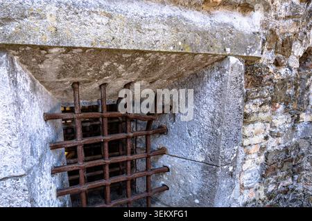 Close view of a rusty iron grate embedded in an ancient stone wall. Architectural detail suitable for history, archaeology, heritage, and travel conce Stock Photo
