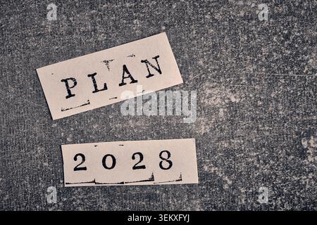 Plan 2028 text printed on paper slips, arranged on dark grey textured concrete background surface Stock Photo