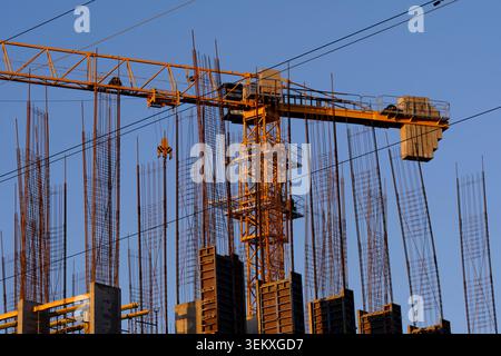 Large yellow industrial crane working on concrete building construction site under blue sky Stock Photo