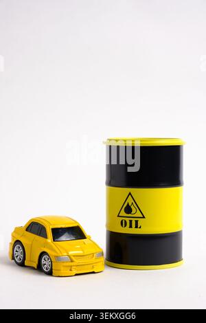 Small yellow toy car standing next to black and yellow oil barrel model on white background Stock Photo