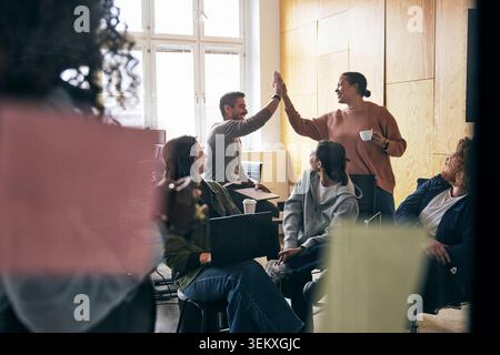 Female tech expert giving high-five to male colleague during office meeting Stock Photo