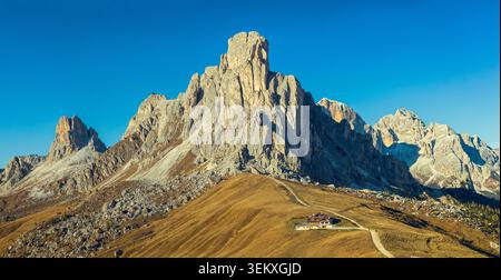 San Vito di Cadore, Italy - 17.10.2021: Rugged limestone cliffs and rocky summits overlooking a small mountain hut on sunlit grassy hills Stock Photo