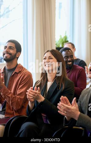 Smiling businesswoman clapping while attending seminar with colleagues in convention hall Stock Photo
