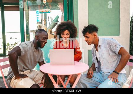 Multicultural startup team enjoys a relaxed outdoor meeting, collaborating over a laptop, having fun Stock Photo
