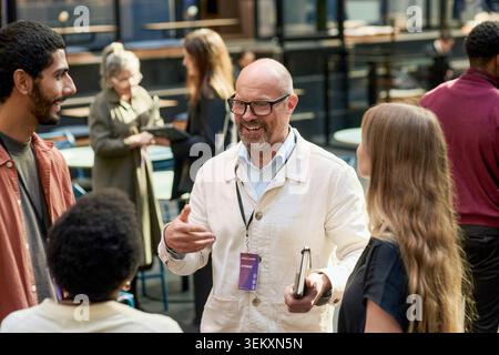 Smiling senior businessman networking with entrepreneurs at event in convention center Stock Photo
