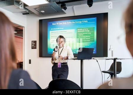 Smiling female business professional holding microphone while addressing audience and giving presentation at seminar in Stock Photo