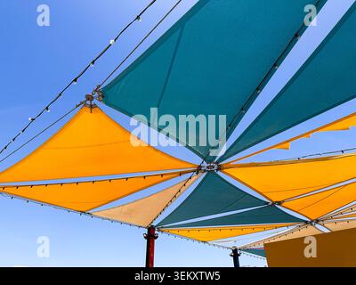 Vibrant yellow and teal striped umbrella with decorative white tassels open under bright sunlight, creating a cheerful summer atmosphere. Stock Photo
