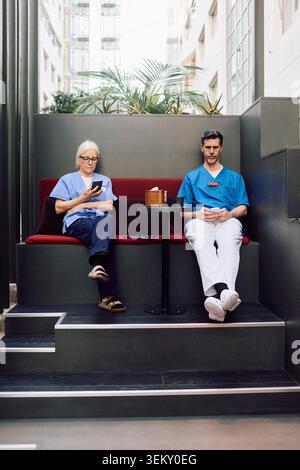 Full length of male and female healthcare workers using wireless technologies during coffee break in modern hospital spa Stock Photo