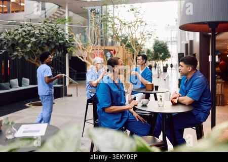 Senior medical professional talking with male coworker while sitting at table in hospital cafeteria during coffee break Stock Photo