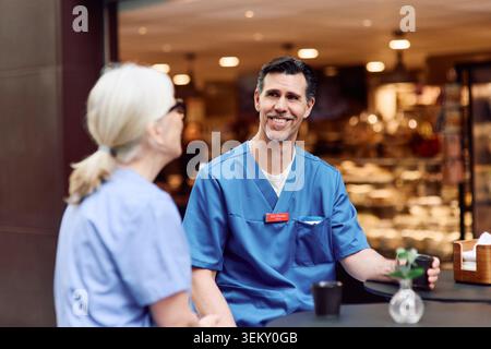 Smiling male healthcare expert talking with senior female coworker during coffee break in hospital cafeteria Stock Photo