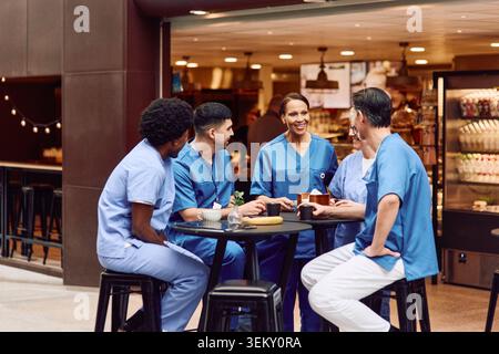 Team of medical professionals talking with each other while sitting at table in hospital cafeteria Stock Photo