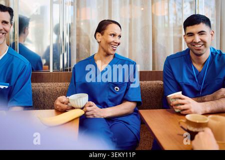 Happy senior female nurse having coffee with male coworkers in hospital cafeteria Stock Photo