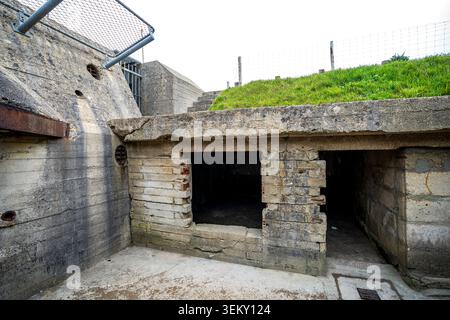 Front view of the open entrances of a concrete bunker at Pointe du Hoc. The structure features raw fortified walls, a grassy roof, side stone stairs, Stock Photo