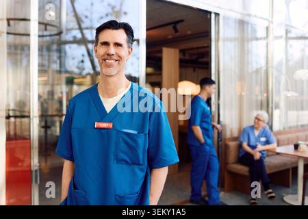 Smiling portrait of mature male physician standing with hands in pockets Stock Photo