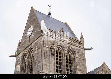 A close-up view of the stone bell tower of the Sainte-Mère-Église church, Normandy. The photo highlights the dummy of paratrooper John Steele hanging Stock Photo