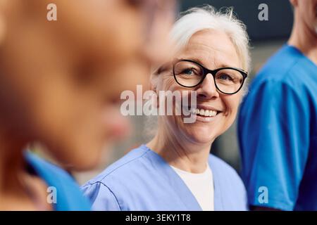 Smiling senior female physician wearing eyeglasses talking with colleague Stock Photo