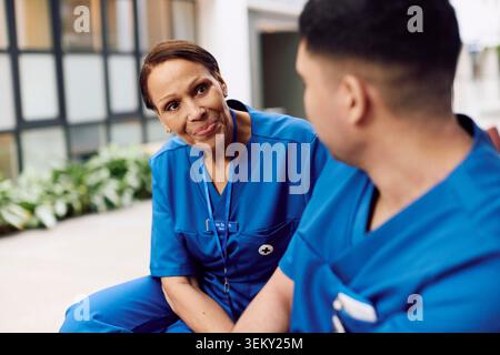 Smiling senior female physician consoling male coworker while sitting in hospital lobby Stock Photo