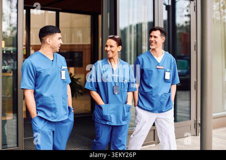 Smiling male and female medical experts walking with hands in pockets outside hospital building Stock Photo