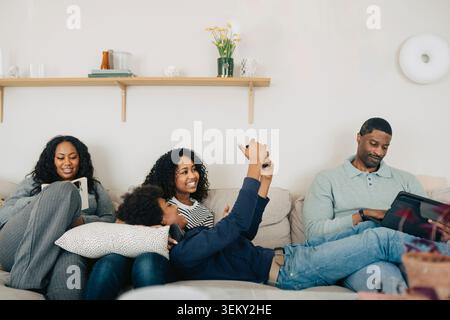 Happy family spending quality time together while using different electronic devices at home Stock Photo
