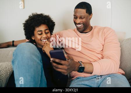 Happy father and son spending quality time with each other using smart phone at home Stock Photo
