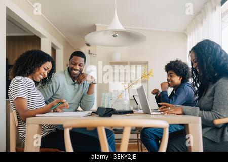 Happy family balancing professional work and kids education while sitting at same table Stock Photo