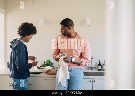 Son helping father while preparing food in kitchen at home Stock Photo