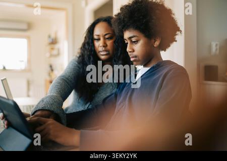 Woman assisting boy doing studies through tablet PC at home Stock Photo