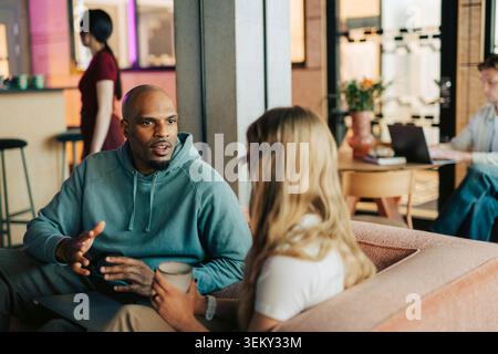 Diverse colleagues having serious discussion while sitting on couch in office lounge Stock Photo