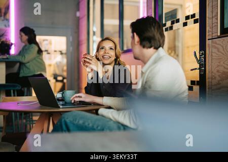 Smiling businesswoman having conversation with male colleague at modern coworking space Stock Photo