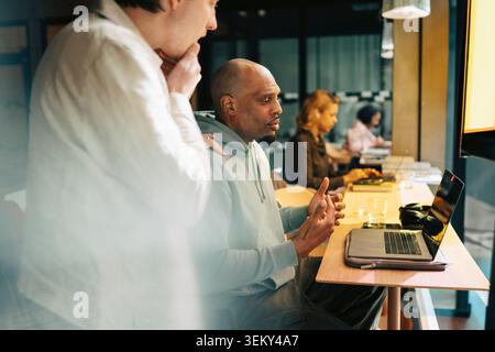 Two male colleagues discussing project on laptop in modern coworking space Stock Photo