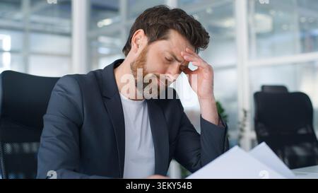 Sad exhausted Caucasian business man with papers hard work suffering with burnout problem paperwork mistake low stats European middle-aged businessman Stock Photo
