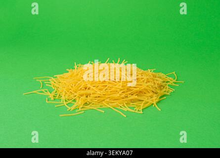 Raw vermicelli on green background, gold soup pasta pile, small homemade noodles, thin macaroni, Italian yellow filini pasta Stock Photo