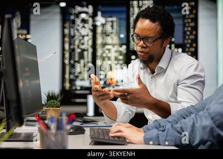 Technicians chatting in startup office, coding advanced machine learning models enhancing automation. Silicon Valley workplace IT specialists discussing, using AI on computer at desk Stock Photo