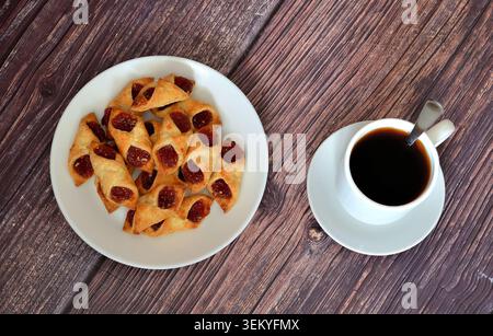 Fogotini puff pastry cookies with jam in a round plate and a cup of hot black tea on a wooden table. Top view, flat lay. Stock Photo