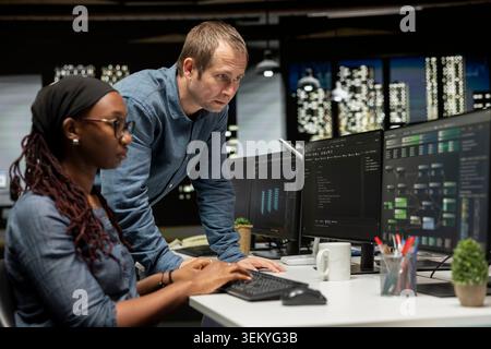Manager discussing with tech startup admin coding AI algorithms on PC. System administrator having conversation with IT professional in office using deep learning models to do automation Stock Photo