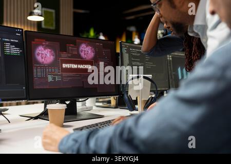 Team of technicians in office working together to fix hacking attempt on corporate network. IT staff members investigating unauthorized access alerts, brainstorming ways to mitigate damages Stock Photo